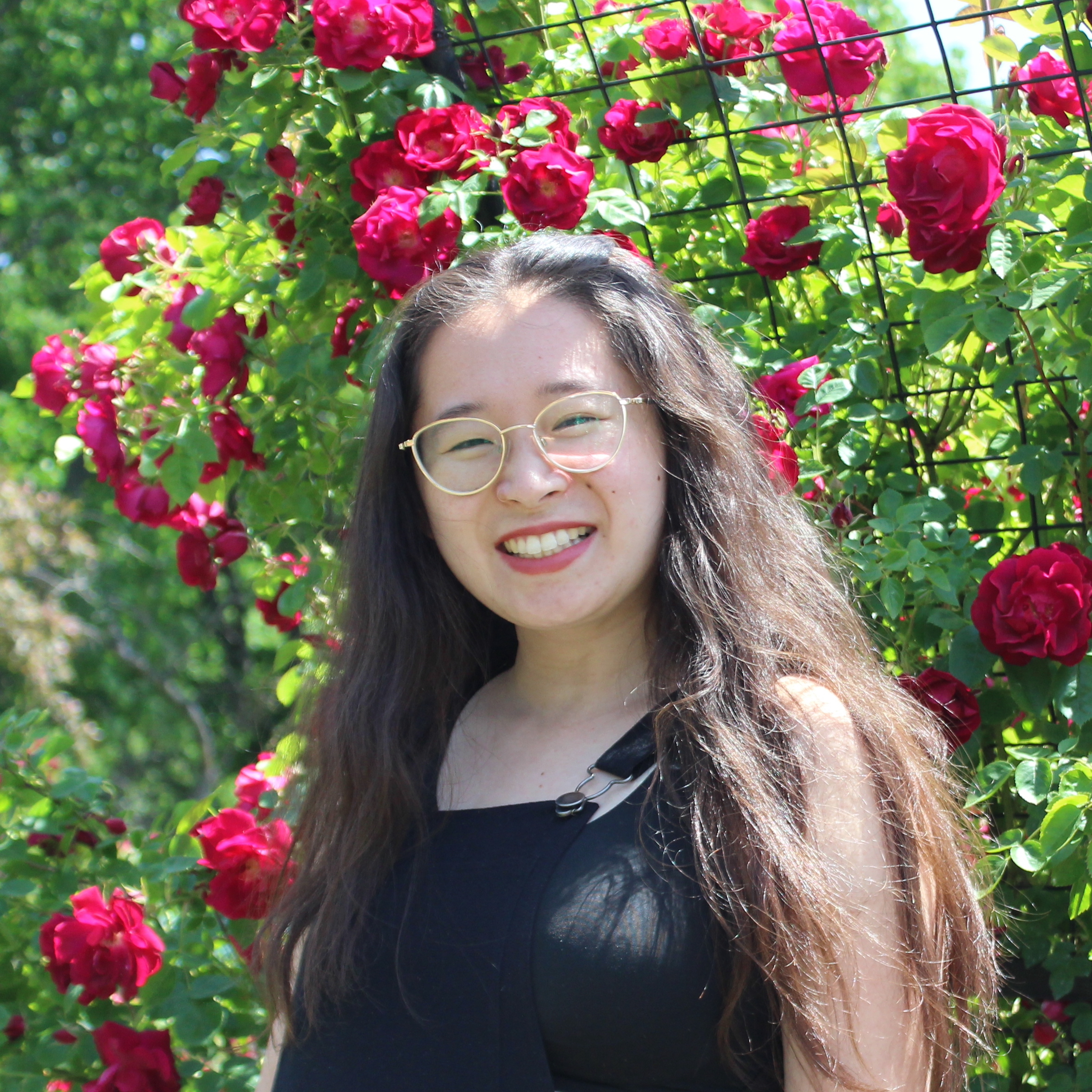 A portrait of Lucy Qin smiling in front of a rose bush